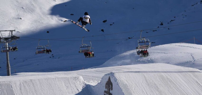 Snowboarder sautant en l'air sur une rampe enneigée.