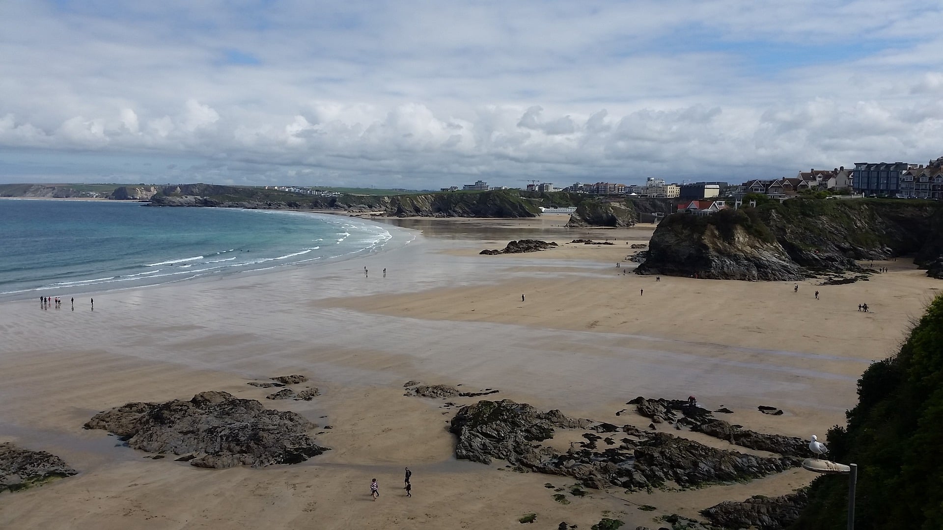 Plage Newquay, Cornouailles avec falaises rocheuses et bâtiments.