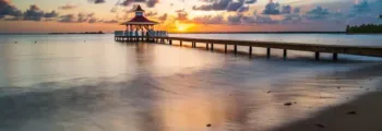 Coucher de soleil sur plage avec jetée en bois.